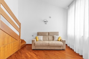 Ein Zimmer mit einer Holztreppe, einem beigen Sofa mit Kissen und einer geometrischen Wanddekoration.