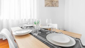 Une table à manger dressée avec des assiettes, des verres et des couverts, une plante et une œuvre d’art murale.