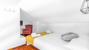 Una habitación de hotel moderna con una cama, una silla roja, una manta amarilla y una lámpara con forma geométrica.