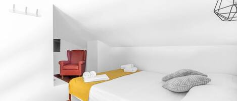 A modern hotel room with a bed, a red chair, a yellow blanket, and a geometric light fixture.