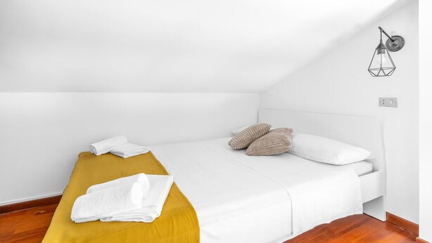 Un lit simple avec une literie blanche, un banc de couleur moutarde et un luminaire fixé au mur.