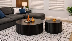 Uma sala de estar moderna com um sofá modular, duas mesas de centro pretas e um vaso de planta.