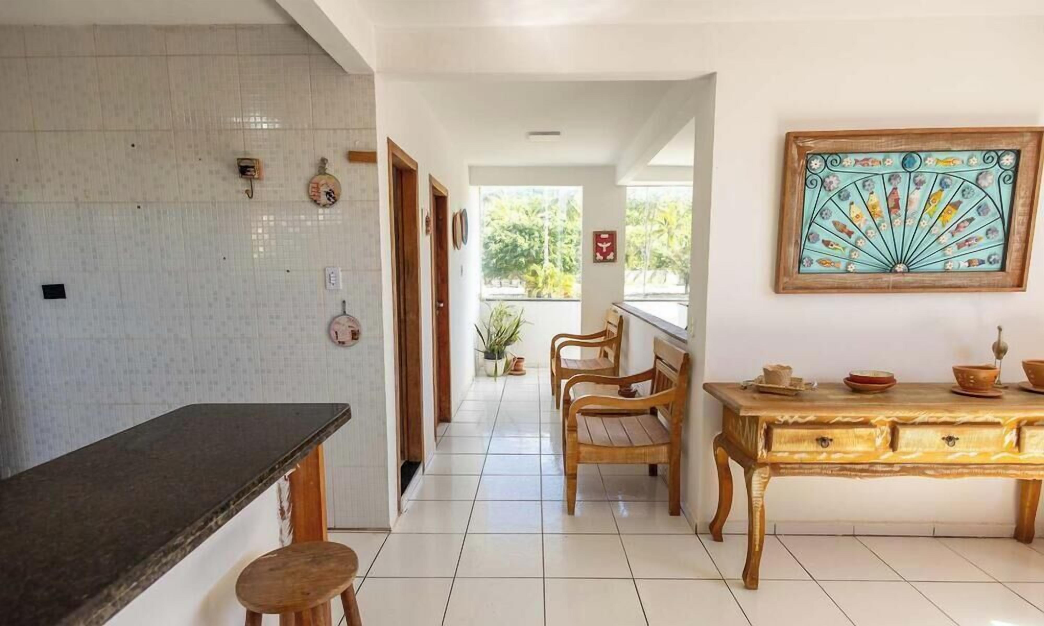 Een keuken met een donker aanrecht, houten stoelen, een houten tafel met kommen, en een decoratieve ventilator aan de muur.