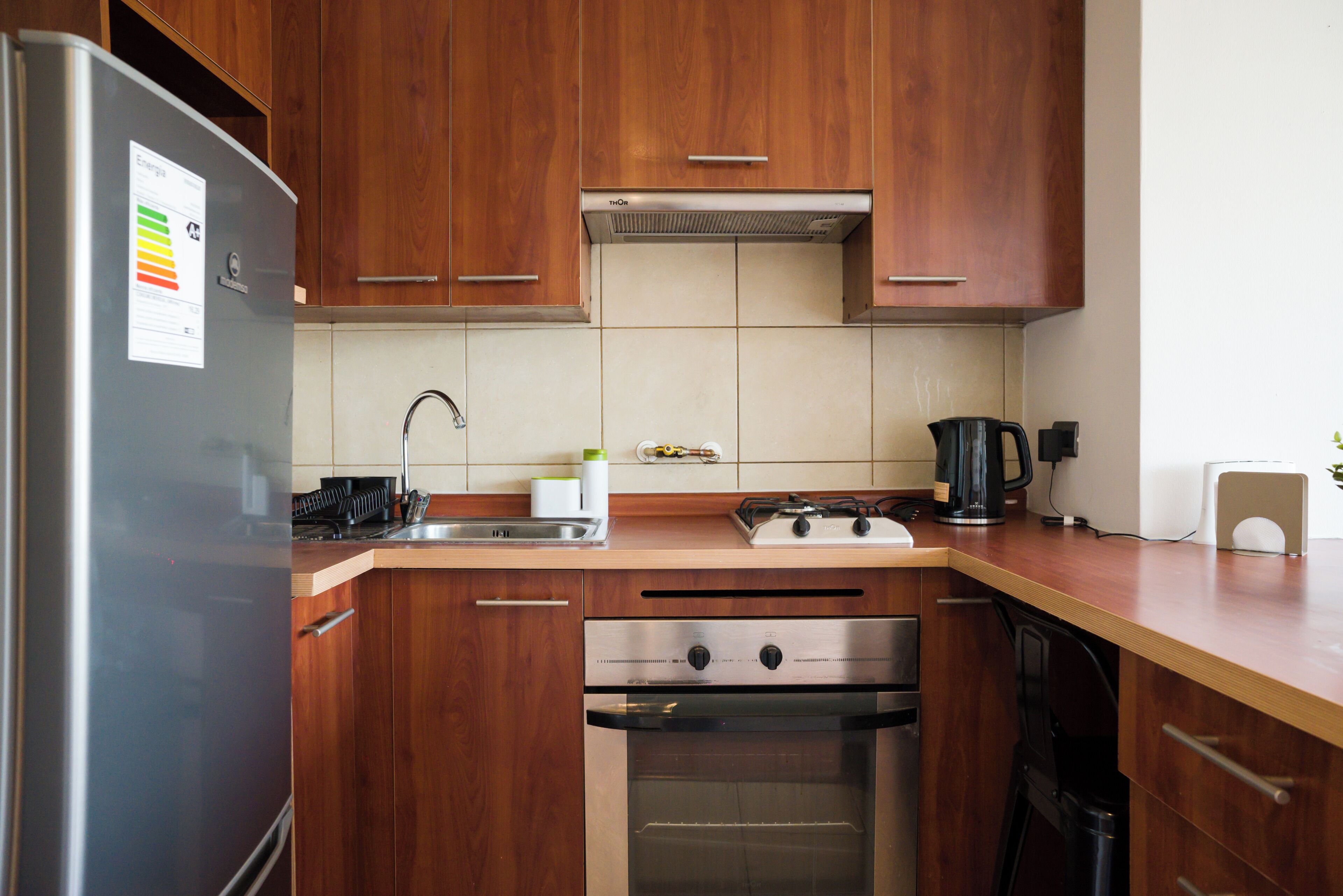 A kitchen with wooden cabinets, a stainless steel refrigerator, a gas stove, an oven, and a sink.