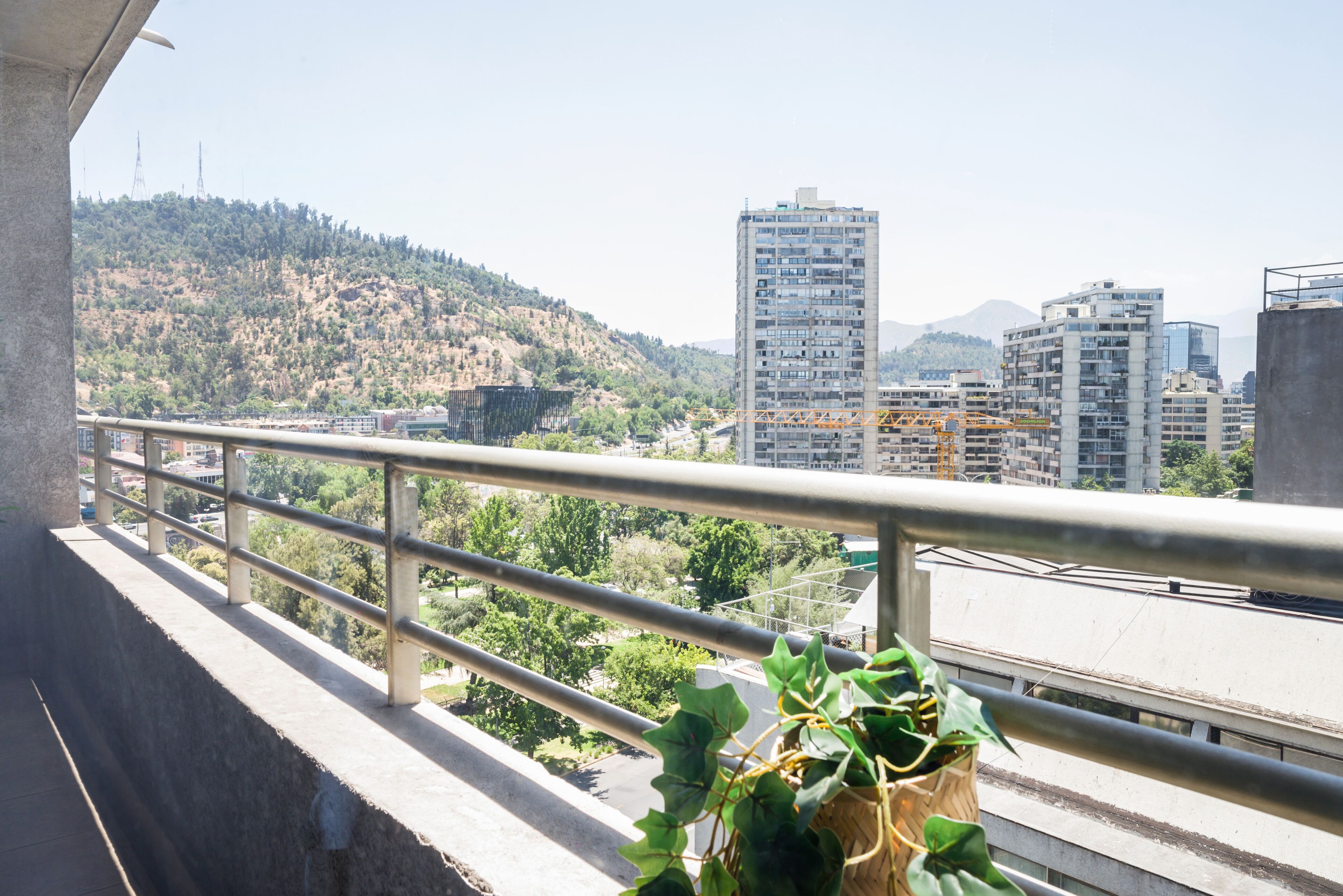 Un balcón con baranda de metal que da a una vista urbana con edificios y colinas.