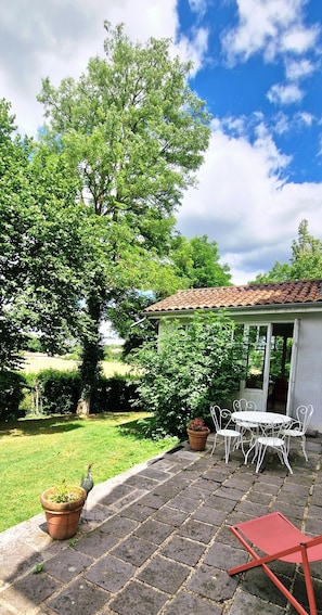 En terrasse med et bord og stole, omgivet af grøn vegetation og en klar himmel.