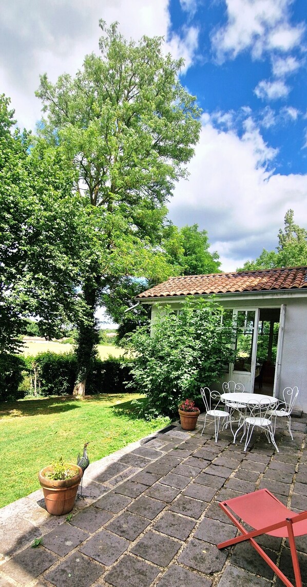 A patio with a table and chairs, surrounded by greenery and a clear sky.