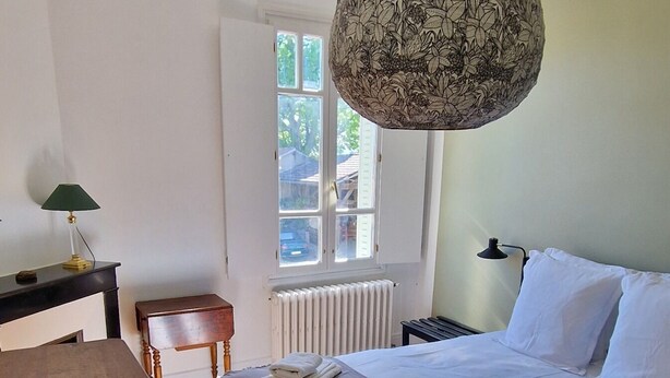 Un dormitorio con una cama de madera, una lámpara colgante, un radiador, una ventana y una mesa de madera.