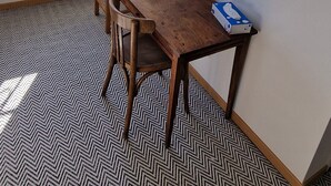 A dining area with a wooden table, two chairs, a window with a view, and a patterned floor.