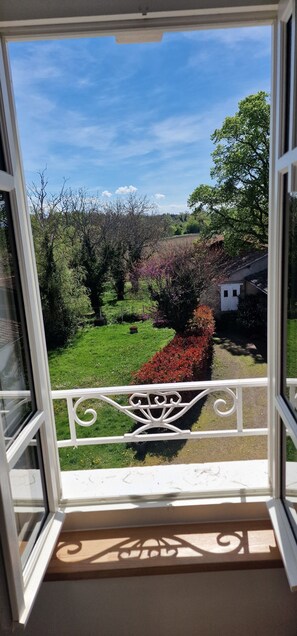 Un balcón con vistas a un jardín, una cerca blanca y un cielo despejado.