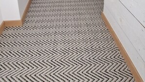 A narrow hallway with a patterned carpet, a wooden horse sculpture, and white walls with wooden paneling.