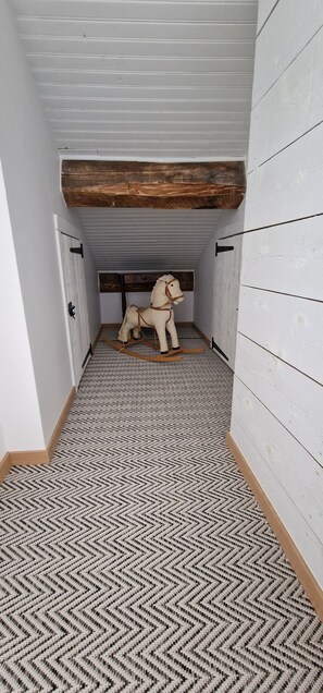 Un pasillo estrecho con alfombra estampada, una escultura de caballo de madera y paredes blancas con paneles de madera.