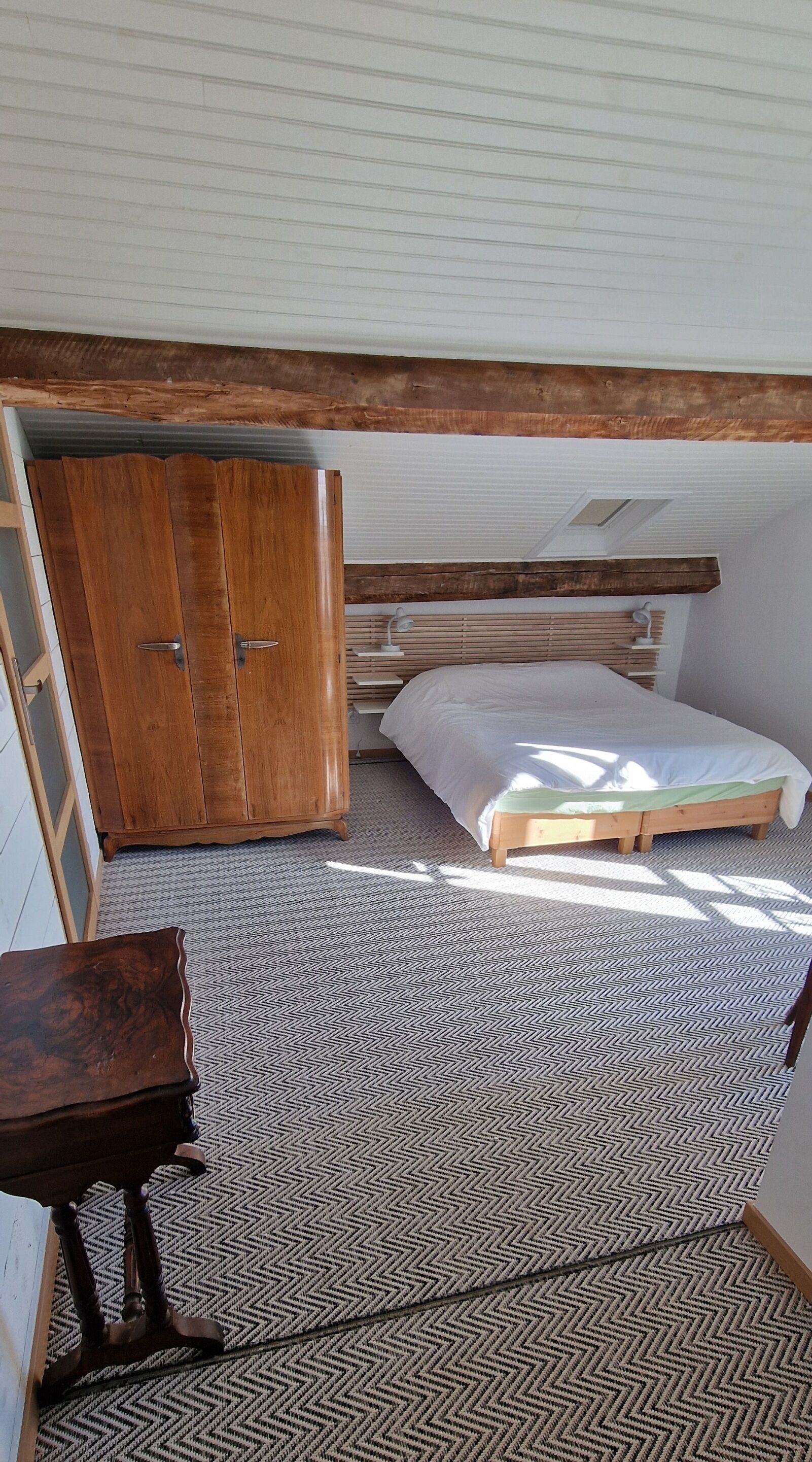 A bedroom with a bed, wooden wardrobe, and a small table.