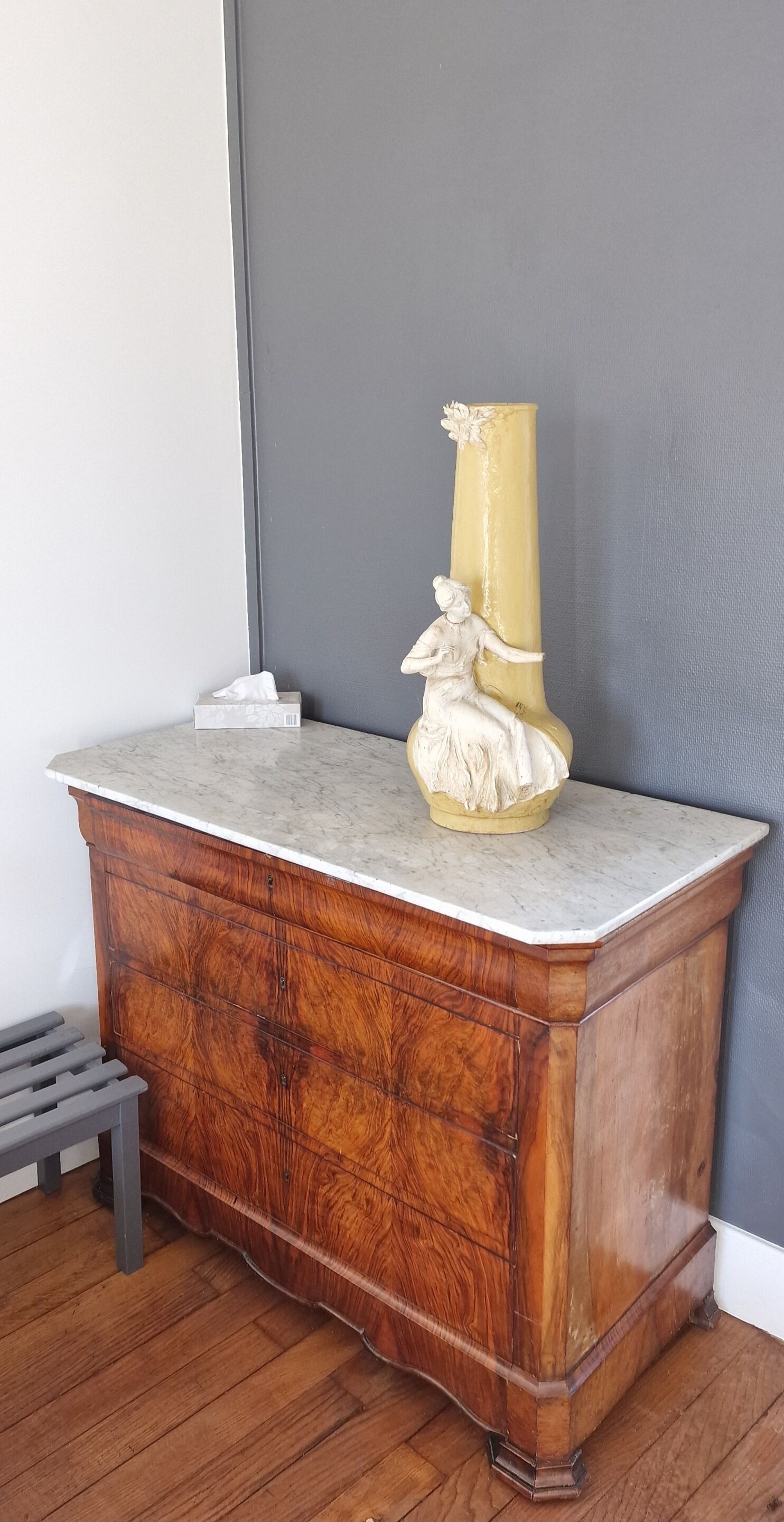 Een houten kast met een marmeren blad, een witte beeldje en een zakdoos.