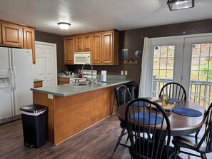 A kitchen with wooden cabinets, a white refrigerator, a microwave, and a sink. There is a dining table with chairs and a window with curtains. - Hilltop Home w/Mtn View,firepit & wifi.Close to DT (Franklin)