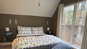 Ein Schlafzimmer mit Bett, Nachttischen, einer Bank und einem Fenster mit Blick auf Bäume.
