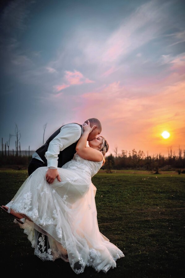 A couple embracing in a field with a sunset in the background.