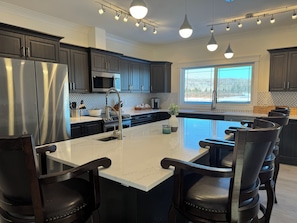 A modern kitchen with dark cabinetry, stainless steel appliances, a large island with seating, and pendant lighting.