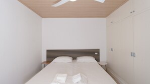 Een keurig opgemaakt bed met witte lakens en handdoeken, een houten plafond en een witte kledingkast met spiegel.