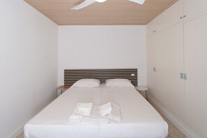 Ein ordentlich bezogenes Bett mit weißen Leinen und Handtüchern, eine Holzbalkendecke und ein weißer Kleiderschrank mit Spiegel.