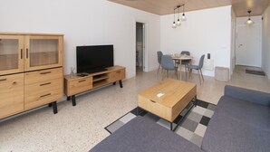 Een moderne woonkamer met een houten kast, een televisie, een salontafel en een eethoek met stoelen.