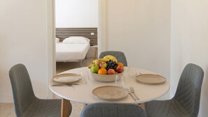 Een eettafel met een fruitschaal, borden, bestek en twee stoelen in een kamer met een bed op de achtergrond.