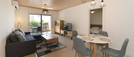 A modern living room with a sofa, coffee table, dining table with chairs, and a TV.