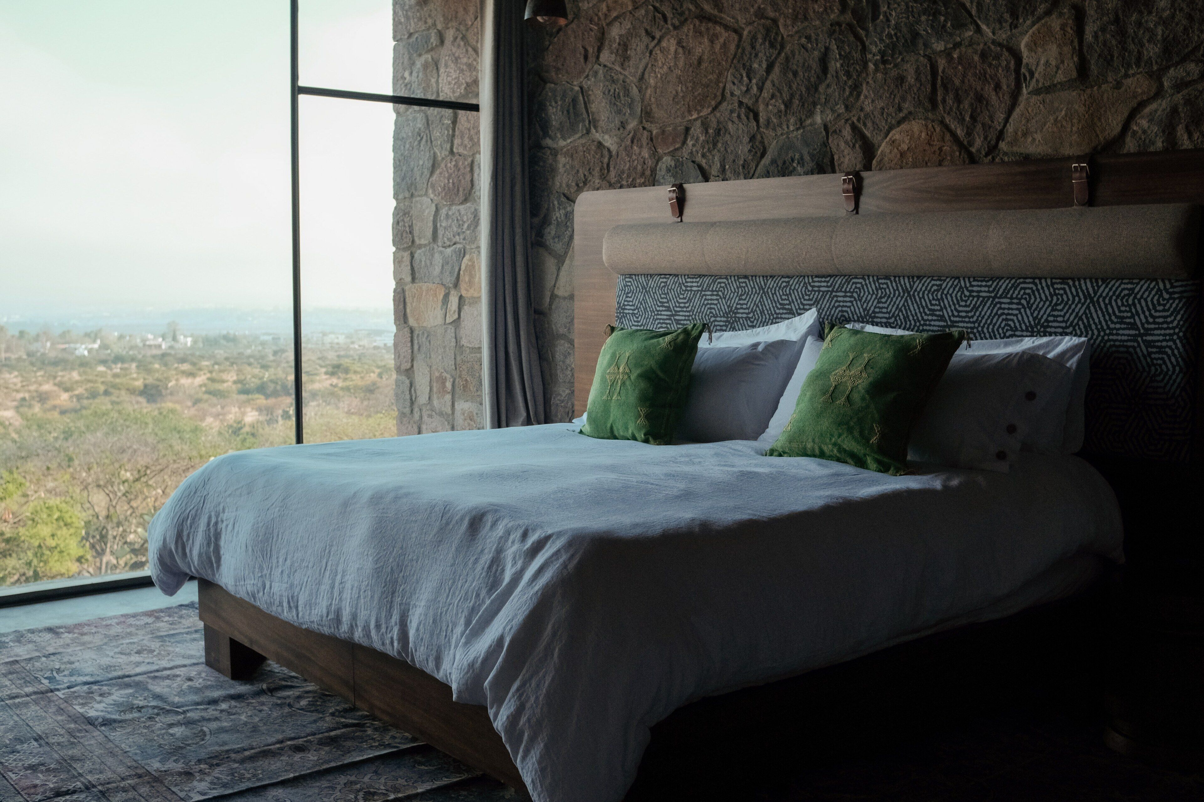 Ein Bett mit Kopfstütze, Kissen und Blick durch ein großes Fenster.
