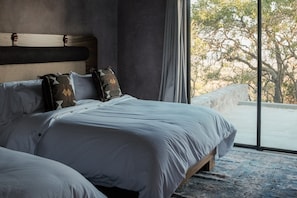 Une chambre avec un grand lit, une tête de lit et une vue sur les arbres par la fenêtre.