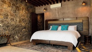 A bedroom with a stone wall, a wooden bed frame, a patterned rug, and a bench.
