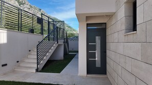 A modern building with a staircase leading to a door, a small lawn, and a mountain in the background. - NEW Villa Lumina/ Pool & Ocean View/ Budva Riviera/ 3-Bedroom for 6 Guests (Rijeka Reževići)