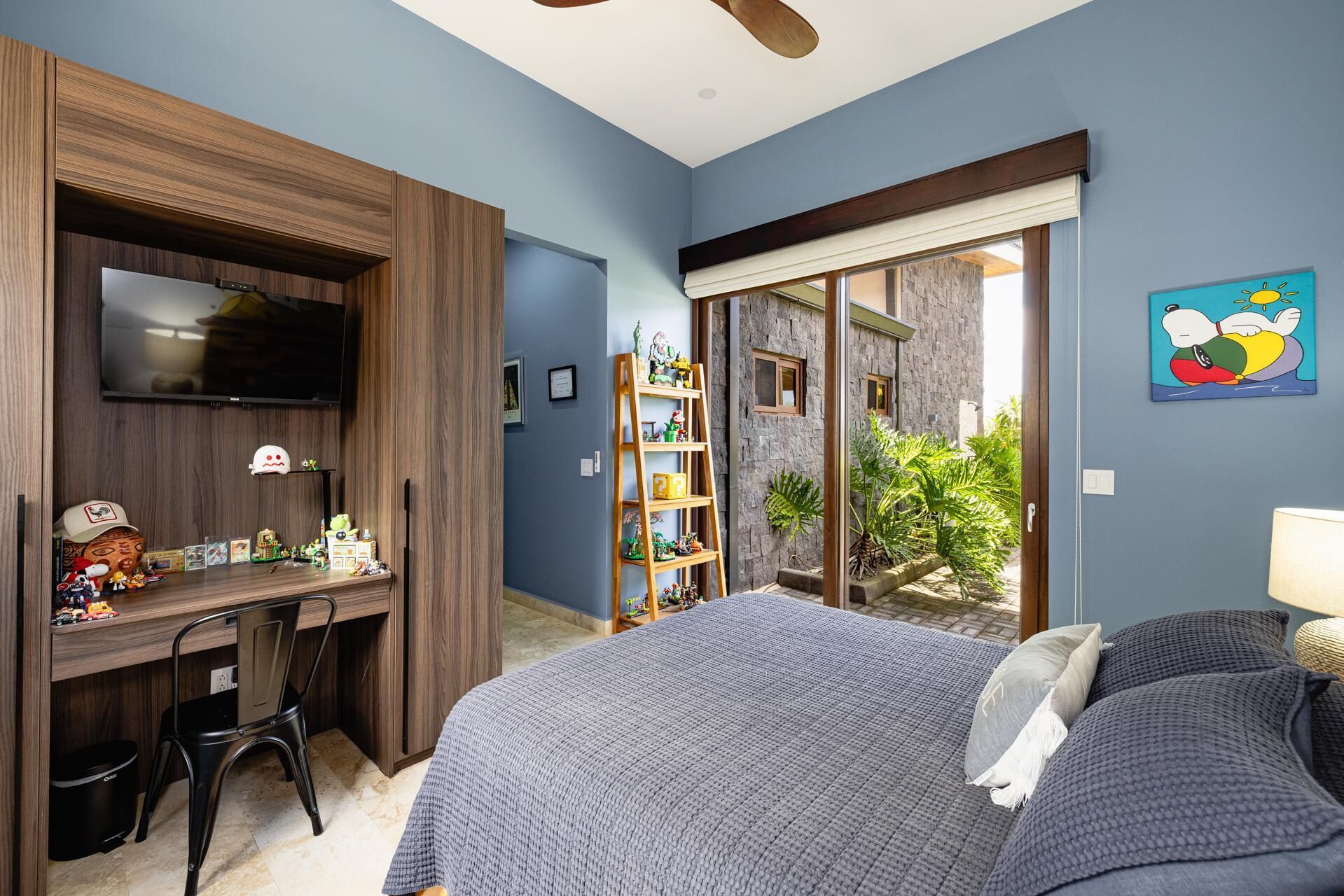 Ein Schlafzimmer mit Bett, Schreibtisch, Fernseher, Bücherregal und Blick ins Freie.