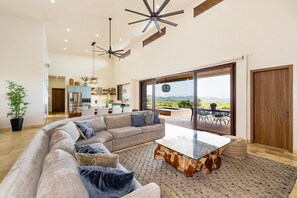 A spacious living area with a large sofa, a glass coffee table, and a view of a mountainous landscape through large sliding doors. - Your Luxurious Ocean view Escape- At Mar Vista (Mar Vista)