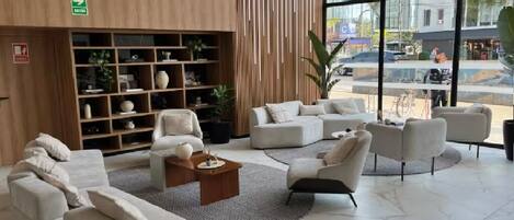 Eine moderne Lobby mit einem Holzbüro, weißen Sofas, einem Couchtisch und einem großen Fenster mit Blick auf die Straße.