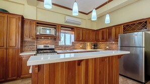 Eine Küche mit Holzausstattung, einem Edelstahl-Kühlschrank, einer integrierten Kücheninsel und Pendelleuchten.