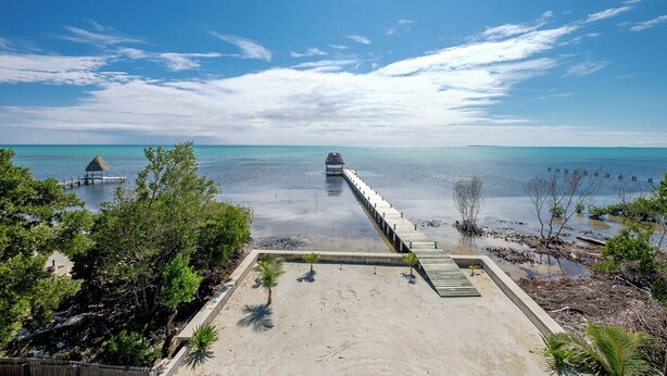 Ein Strand mit einer hölzernen Mole, die ins Wasser hineinreicht, umgeben von viel Grün.
