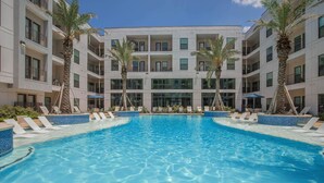 A pool area with lounge chairs and palm trees, surrounded by a multi-story building with balconies. - 5 min from NRG - Pool, Gym & Free Parking (Houston)