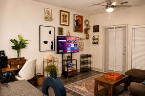 A living room with a flat-screen TV, a sofa, a coffee table, a bookshelf, and a door. - 5 min from NRG - Pool, Gym & Free Parking (Houston)
