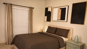 A bedroom with a bed, curtains, a nightstand, and wall art. - 5 min from NRG - Pool, Gym & Free Parking (Houston)