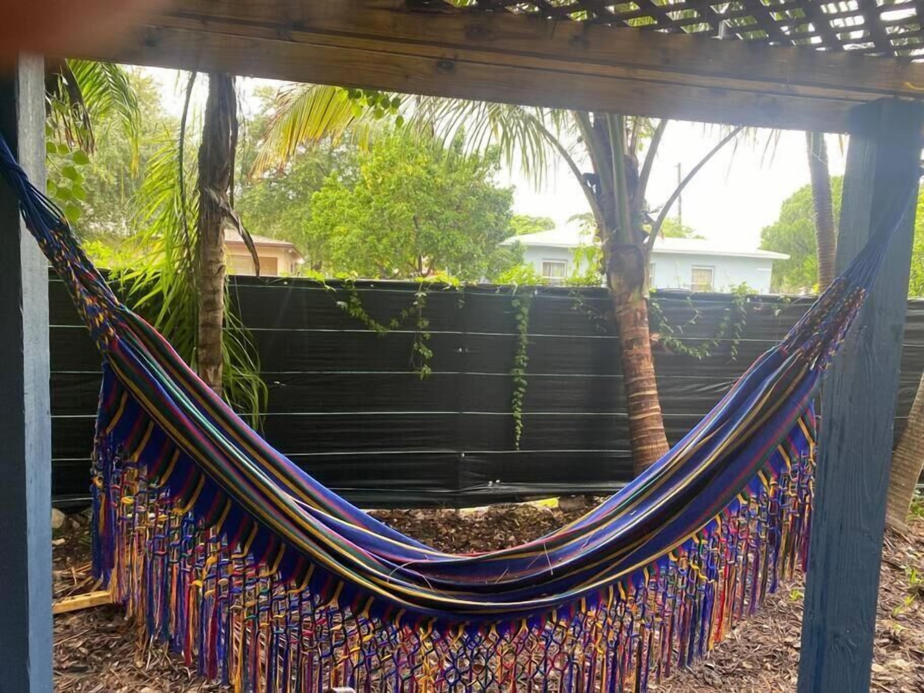 A hammock under a wooden structure with a view of a fence and trees.