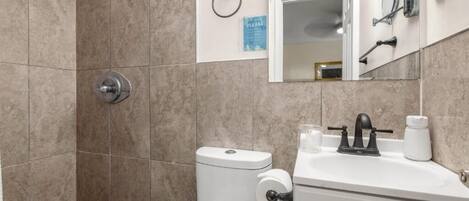 A bathroom with a shower, toilet, sink, and a mirror.