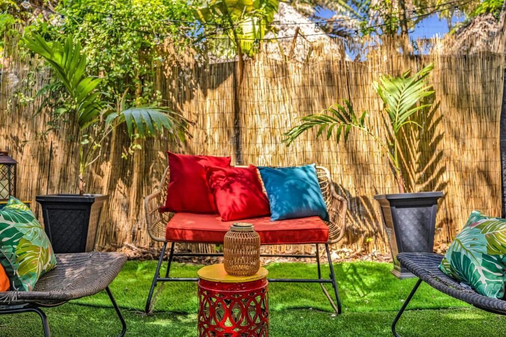 A patio area with a wicker sofa, red and blue cushions, and a small table with a woven centerpiece.