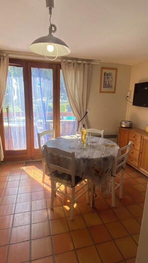 A dining area with a table, chairs, a bottle of wine, and a television on a wooden cabinet. - Appartement avec PISCINE/TENNIS dans petite residence  proche village provencal (Sablet)