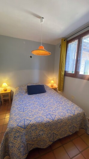 A bedroom with a bed, two bedside lamps, a hanging light fixture, a window with curtains, and a wall-mounted light switch. - Appartement avec PISCINE/TENNIS dans petite residence  proche village provencal (Sablet)