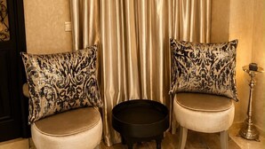 Een kamer met twee gestoffeerde fauteuils, een klein zwart krukje en een decoratieve vloerlamp.