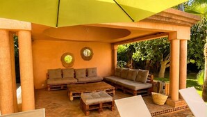 An outdoor seating area with a yellow umbrella, wooden furniture, and a tiled floor. - Escape to Paradise | Exclusive Villa with Pool (Marrakech)