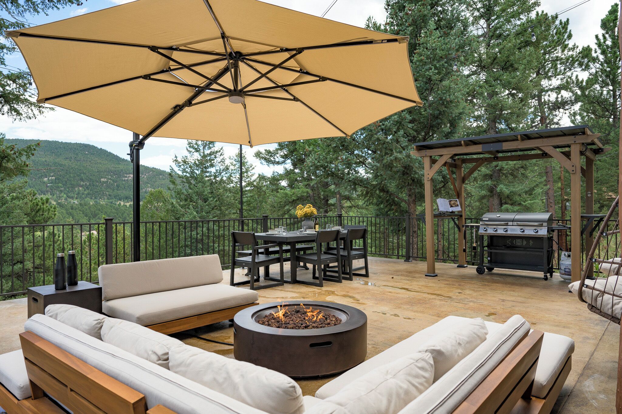 Een terras buiten met vuurkorf, zithoek en een pergola met een barbecue.