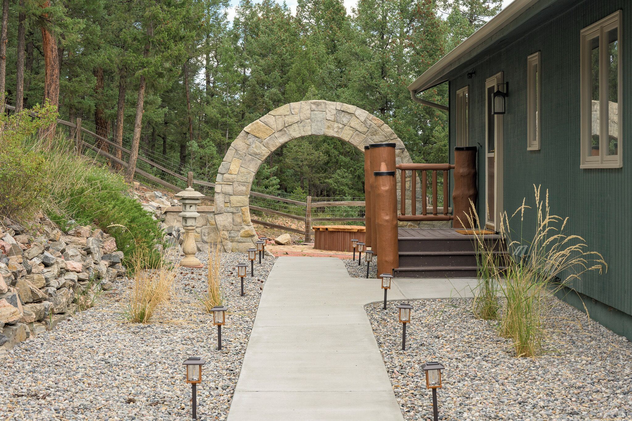 A pathway leading to a stone archway, a wooden deck, and a building with a green exterior.