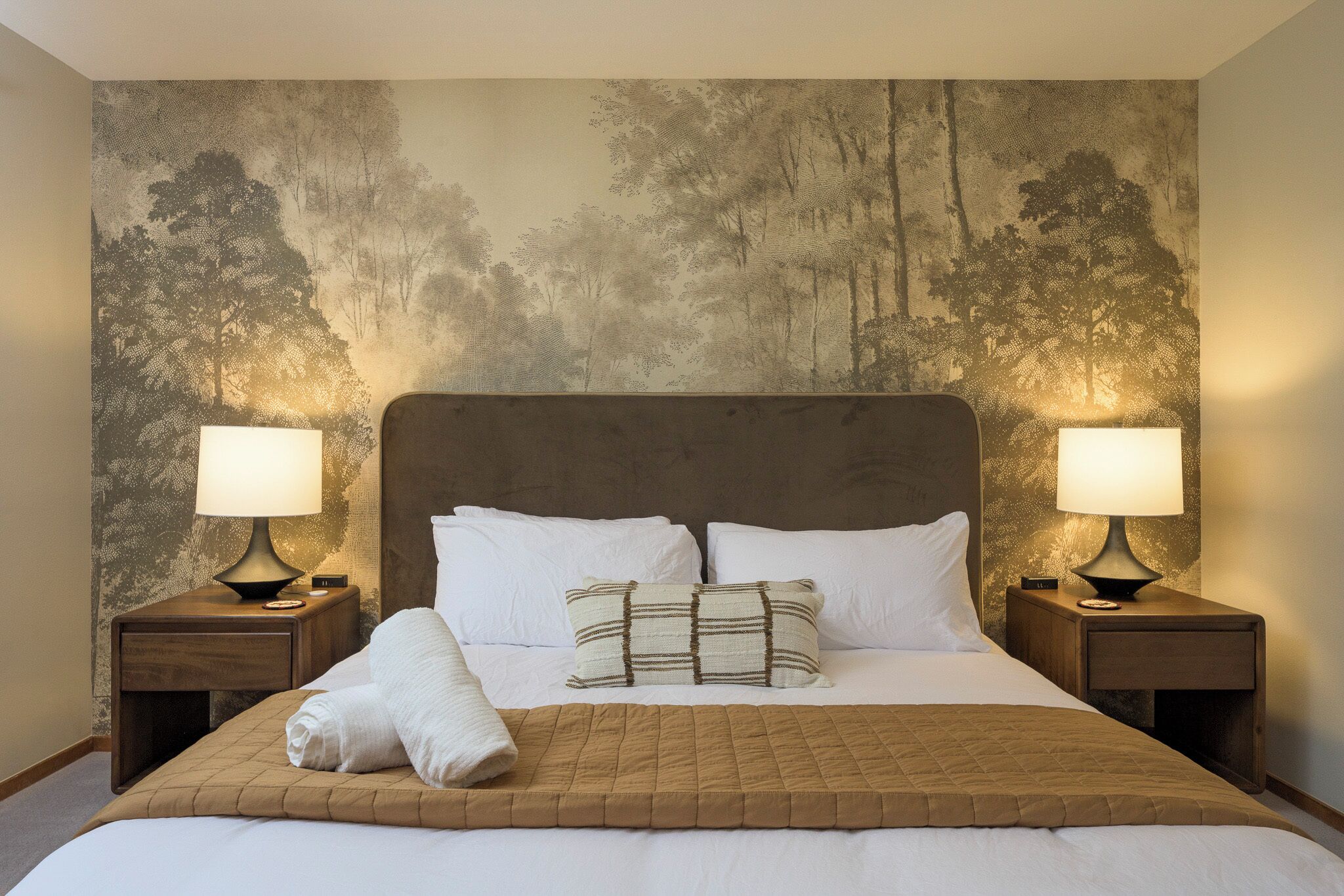 Een hotelkamer met een groot bed, twee bedlampen en een wanddecoratie met een structuur.