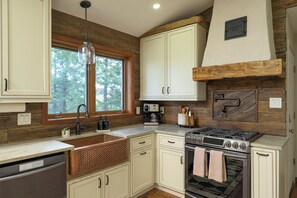 A kitchen with wooden cabinetry, a stainless steel stove, and a window with a view of trees.
